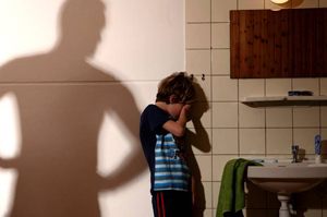 Foto van een jongetje in de badkamer dat bedreigd wordt door een schaduwbeeld